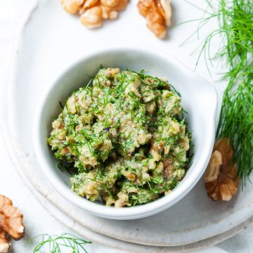 dill pesto in white bowl with fresh dill and walnuts in the background