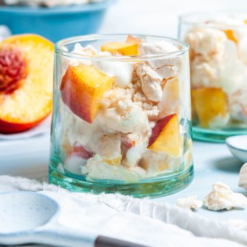 side shot of glass filled with meringue, yogurt and fresh peaches to show the ingredients of peach eton mess