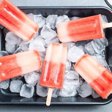 dark baking dish filled with ice, with watermelon ice lollies laid out on the top