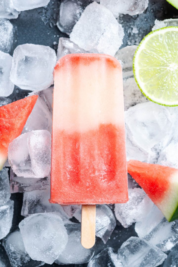watermelon ice lolly on background of ice cubes, with fresh watermelon wedges and slices of lime to show the two ingredients
