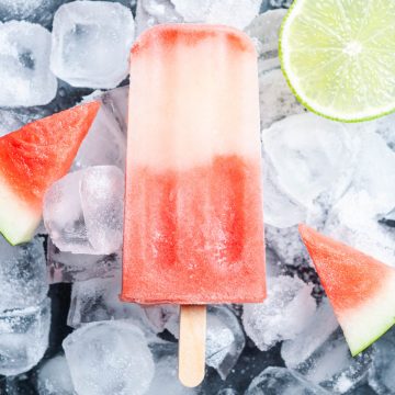 watermelon ice lolly on ice cubers with fresh watermelon wedges and slice of lime at the edges to show the two ingredients