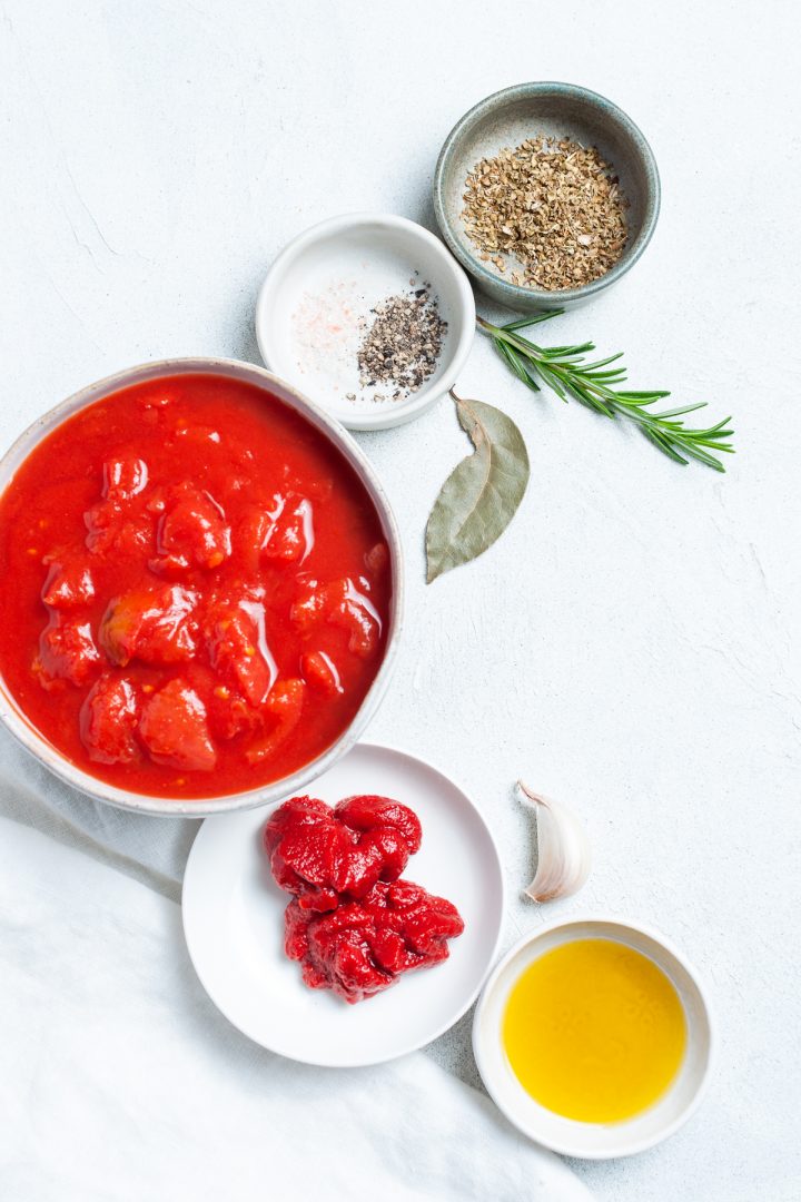 Ingredients for homemade pizza sauce: chopped tomatoes, tomato paste, olive oil, garlic, fresh rosemary, bay leaf, dried oregano, salt and pepper