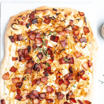 German pizza with bacon and onions on white background, fresh thyme sprinkled over it