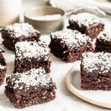 side shot of squares of chocolate fudge slice, the main in focus on a plate, to show the moist cake and chocolate icing layer