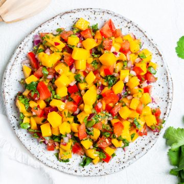 a plate of mango salsa with squeezed lime halves and fresh coriander around the edges
