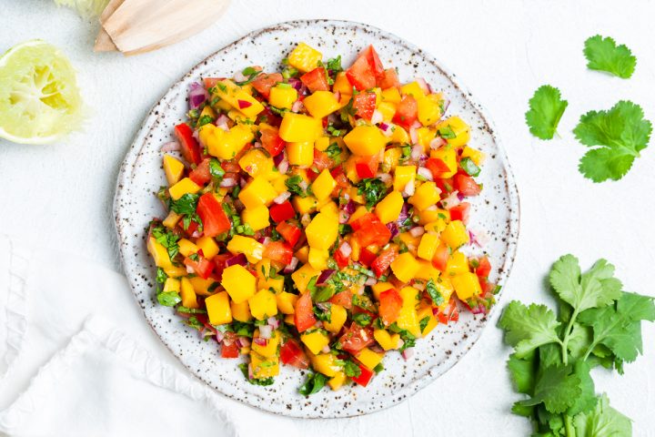 a plate of mango pico de gallo with squeezed lime halves and fresh coriander around the edges