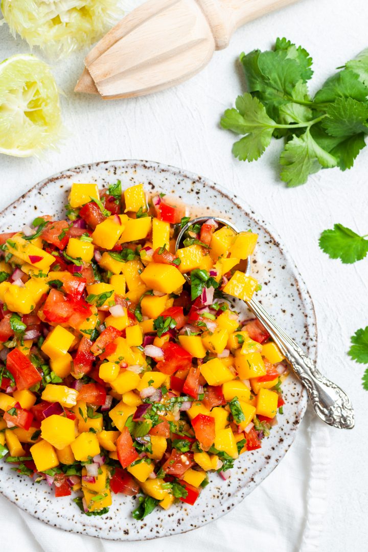mango gallo on a plate with a spoon ready to serve, freshly squeezed lime halves and fresh coriander scattered around