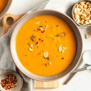 overhead shot of pumpkin peanut butter soup in a bowl sprinkled with peanuts and chilli flakes