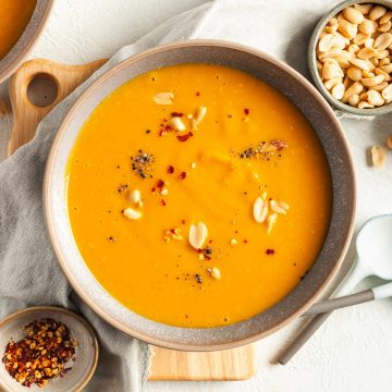 overhead shot of pumpkin peanut butter soup in a bowl sprinkled with peanuts and chilli flakes