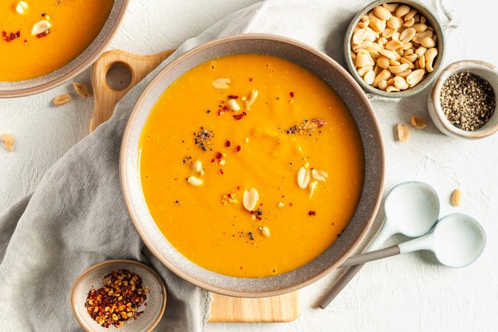 overhead shot of pumpkin peanut butter soup in a bowl sprinkled with peanuts and chilli flakes