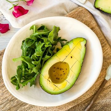 half an avocado in white bowl filled with vinaigrette, served with a handful of fresh rocket