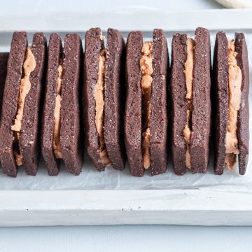angled shot of bourbon biscuits stacked side by side with a spoon of chocolate buttercream to their right