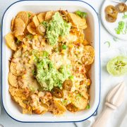 overhead photo of a full dish of tuna nachos topped with mashed avocado and chopped spring onions, lime and jalapenos at the side for those who want them on their nachos