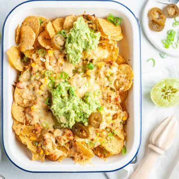 overhead photo of a full dish of tuna nachos topped with mashed avocado and chopped spring onions, lime and jalapenos at the side for those who want them on their nachos