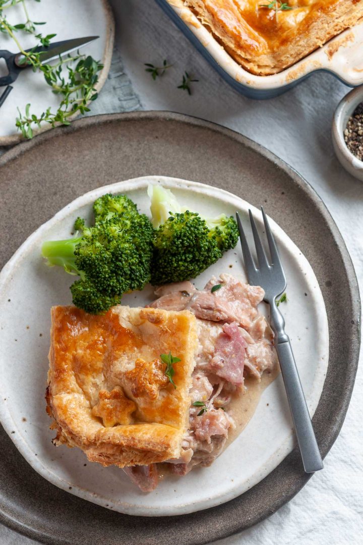 Portion of chicken and ham pie served on a plate with broccoli, the creamy juicy filling visible
