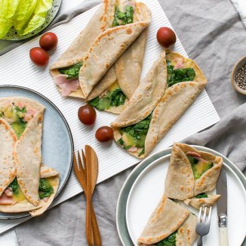 overhead photo of ham and cheese crepes being served, 3 on 2 different plates and a further two on serving board