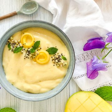 overhead shot of mango smoothie bowl in blue bowl scattered with chia seeds, mint leaves and fresh mango