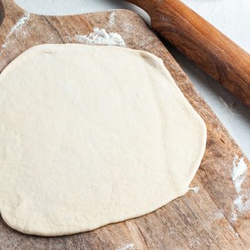 pizza dough rolled out into a circle on wooden board, ready for pizza toppings