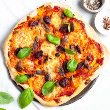 Pizza puttanesca sprinkled with basil leaves