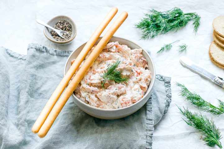 bowl of smoked salmon pate with two breadsticks on the side of the bowl, ready to dip into the salmon