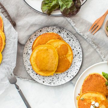 savoury pumpkin pancakes on two plates, one left plain, the other served with salad and topped with feta