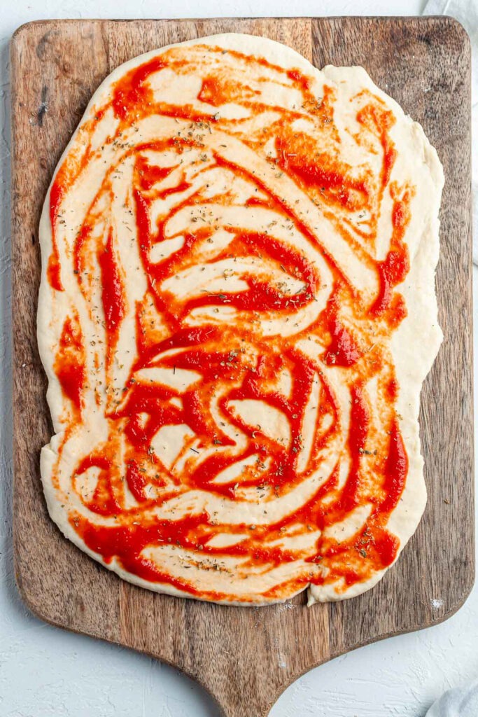 The dough rolled out and spread with tomato sauce.