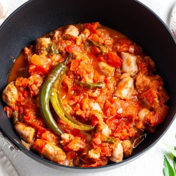 a saucepan of sausage rougaille topped with a whole chilli, curry leaves and tomatoes just visible behind