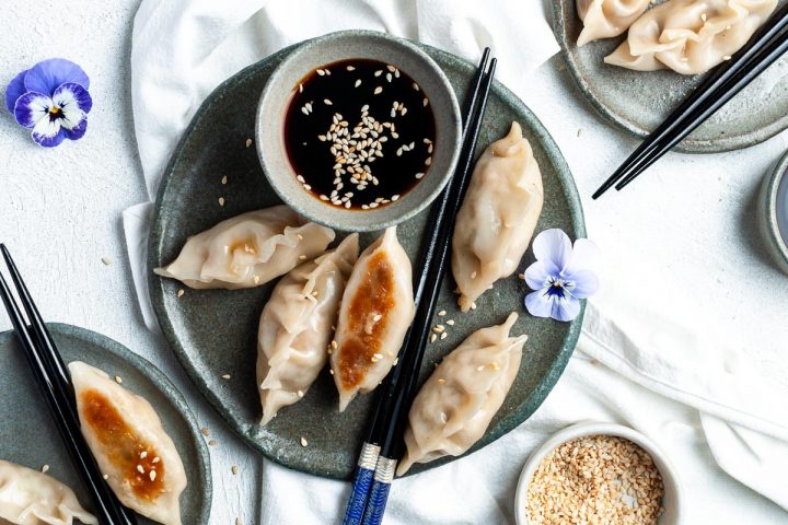 mushroom gyoza on dark blue plate next to a small bowl of dipping sauce, sesame seeds sprinkled over the top and a pair of chopsticks on the side