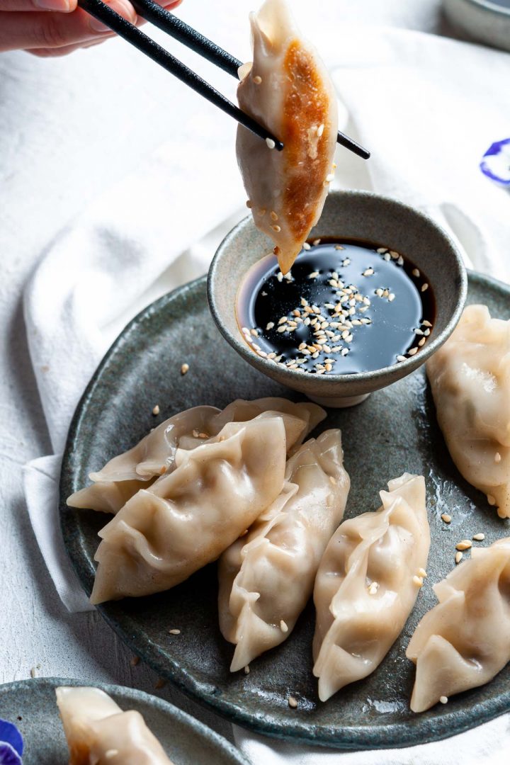 Japanese dumplings held with chopsticks being dipped into the dipping sauce, the crispy golden bottom showing,