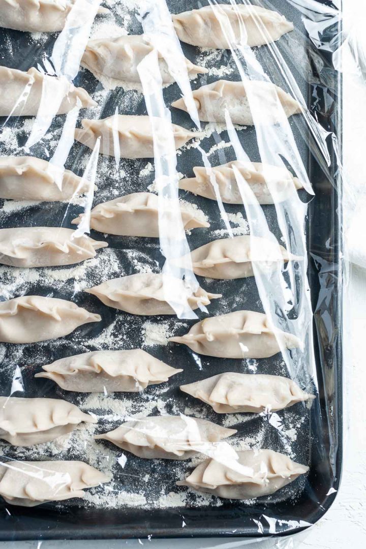 photo of how to freeze potstickers, placed on floured tray and covered with cling wrap