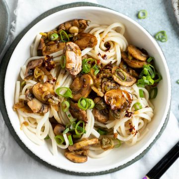 vegan dan dan noodles in a white bowl, more homemade chilli oil to the left ready to drizzle over