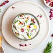 mast o khair in a small bowl on a plate decorated with dill, olive oil and edible rose petals