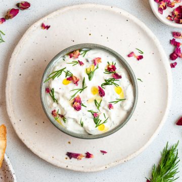 mast o khair in a small bowl on a plate decorated with dill, olive oil and edible rose petals