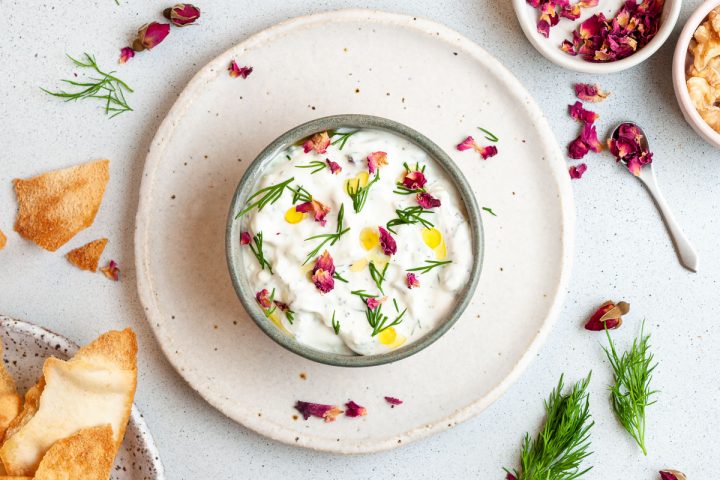 mast o khair in a small bowl on a plate decorated with dill, olive oil and edible rose petals