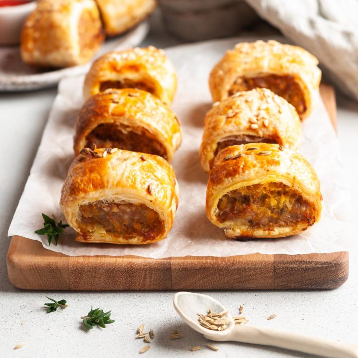 side view of pork and apple sausage rolls to show the filling, as spoon of fennel seeds and fresh thyme leaves in front
