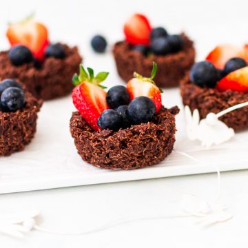 side view of shredded wheat nests filled with berries on a white background
