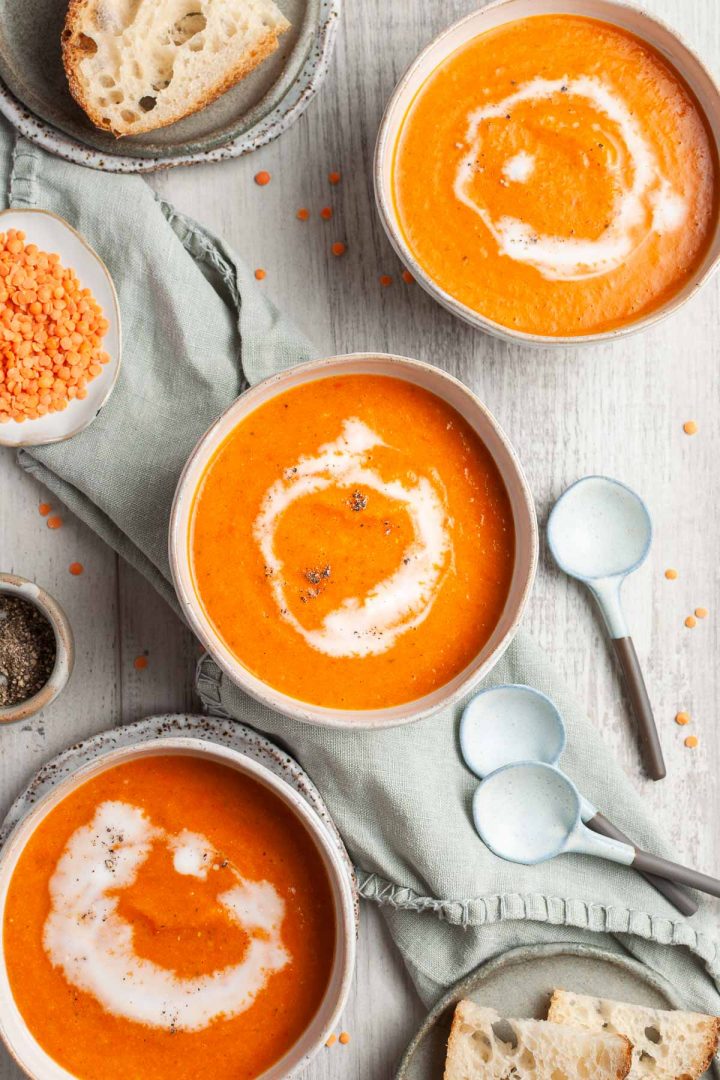 three bowls of carrot and lentil soup swirled with coconut milk, slices of bread just visible ready to dunk into the soup