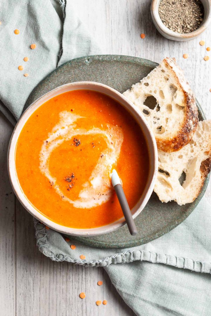 spiced carrot lentil soup in bowl with spoon, served wth bread on the side ready to dip into the soup