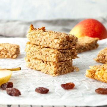 a stack of 3 flapjacks on white paper on cooling rack, surrounded by pears and raisins