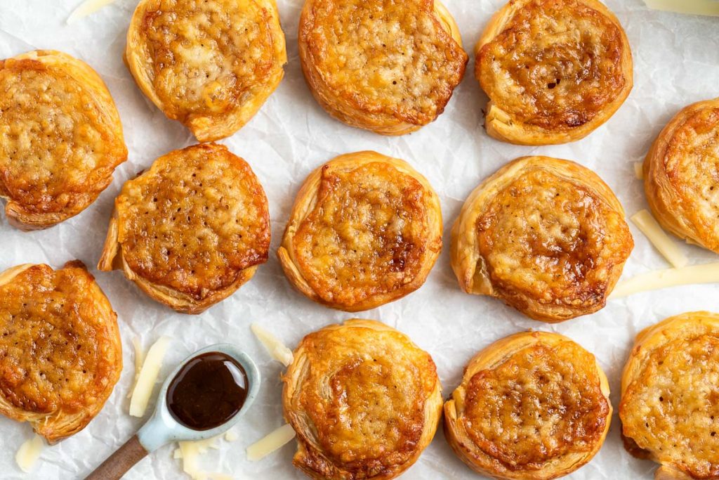 overhead photo of baked cheese and marmite pinwheels on white background, grated cheese sprinkled around them and a spoon of marmite just visible