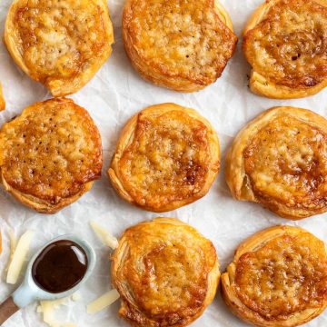 overhead photo of baked cheese and marmite pinwheels on white background, grated cheese sprinkled around them and a spoon of marmite just visible