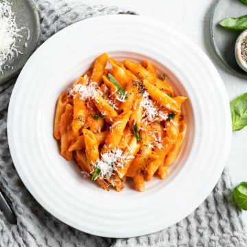overhead bowl of a white bowl filled with penne pomodoro sprinkled with grated parmesan, black pepper and fresh basil