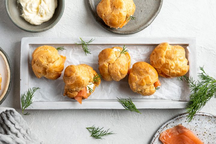 overhead photo of 5 savoury profiteroles on a rectangular grey plate, decorated with fresh dill.