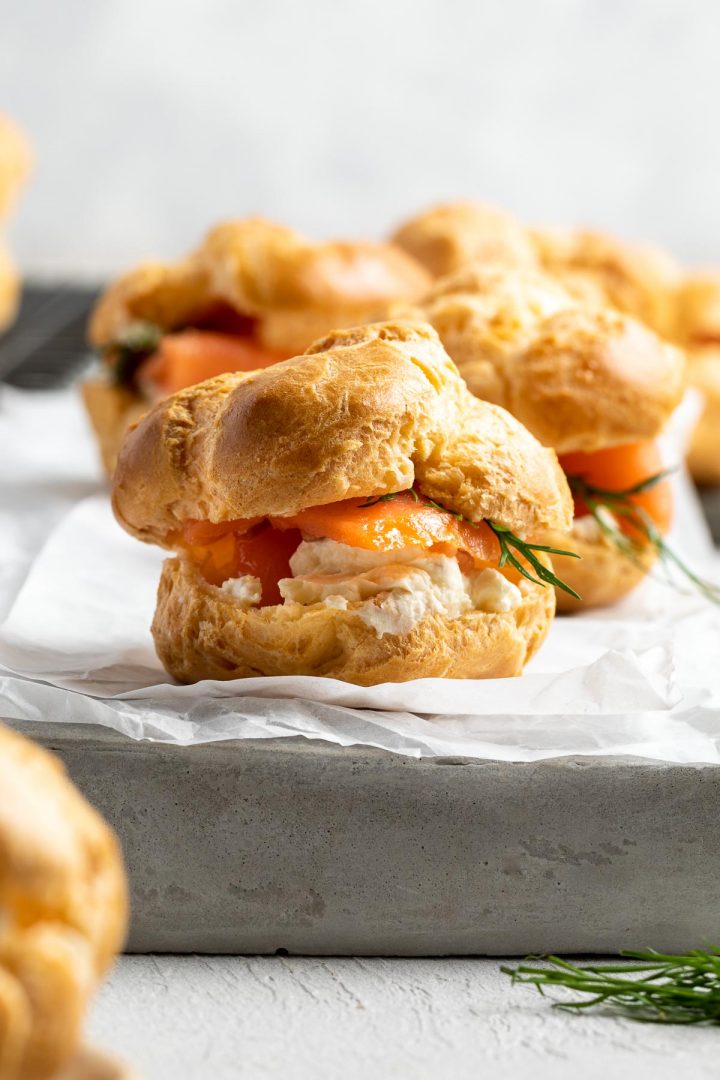 close up side view of savoury profiterole on a grey plate, filled with slices of smoked salmon, cream cheese and fresh dill