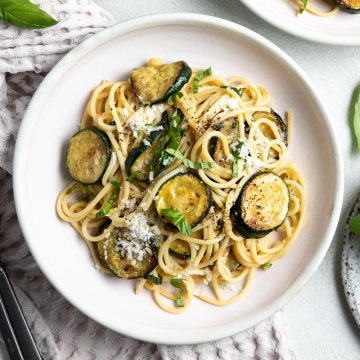overhead photo of a light pink bowl of spaghetti with courgettes, sprinkled with parmesan and fresh basil