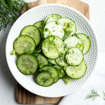 German cucumber salad ready tp serve on a white plate, extra fresh dill sprinkled around the side
