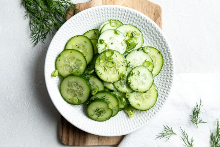 German cucumber salad ready tp serve on a white plate, extra fresh dill sprinkled around the side