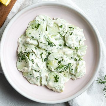 overhead photo of creamy cucumber salad in a pale pink bowl, sprinkled with fresh dill