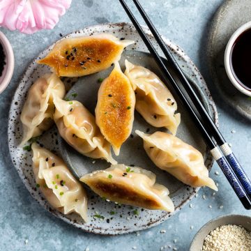 overhead photo of veggie gyoza on a plate served with soy sauce, two dumplings upside down to show their golden crispy base