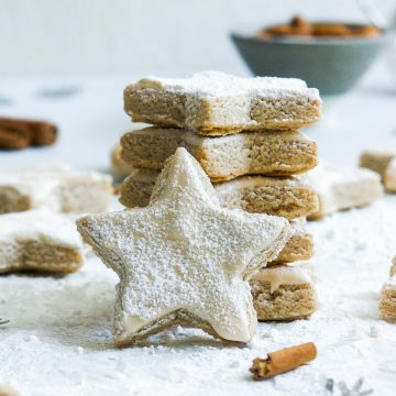 a stack of cinnamon star biscuits, with one zimtsterne on its edge to show the meringue icing